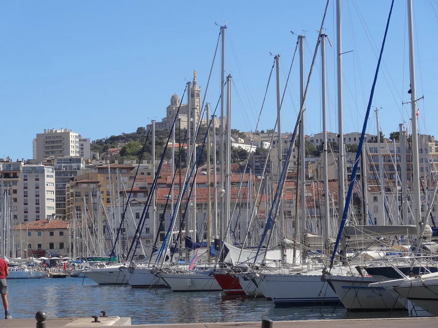 Bateaux amarrés au Vieux-Port de Marseille, devant les immeubles du quai et Notre-Dame de la Garde.