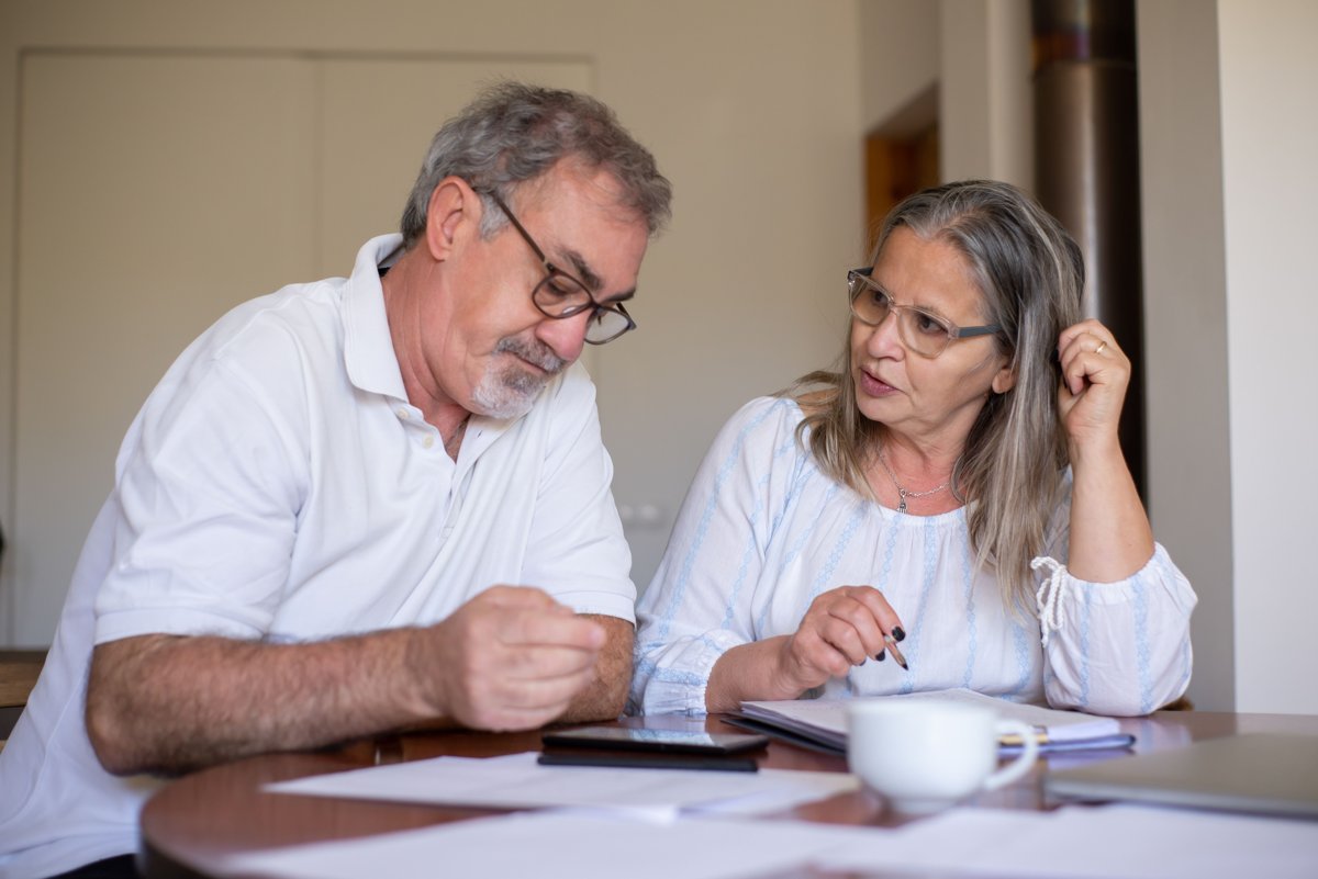 Deux personnes âgées examinent des documents à une table, photographie illustrative de la préparation d’une transmission.