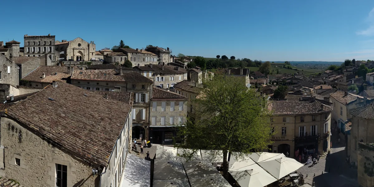 Vue de Saint-Émilion en Gironde, avec les toitures du bourg au premier plan et le paysage viticole à l’horizon.