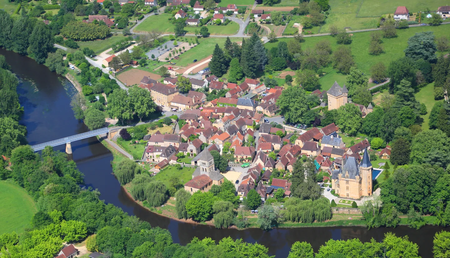 Vue aérienne de Saint-Léon-sur-Vézère : village, pont et rivière entourés de verdure, en Dordogne.